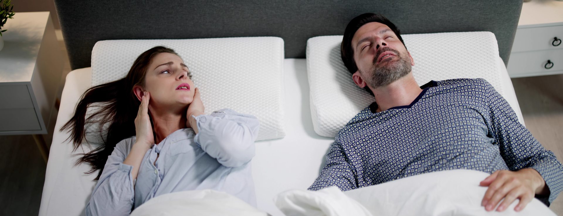 Photo of a woman and man in bed and the woman covering her ears