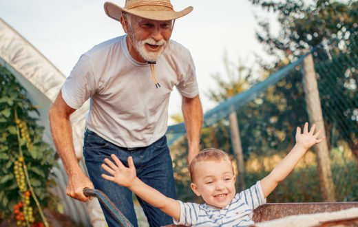 A man pushing a wheelbarrow with a child sitting inside, both smiling happily.