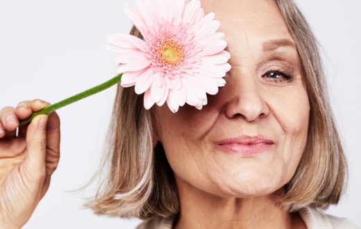 Senior woman managing menopause holding a pink flower to her eye.