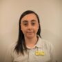 Headshot of a woman with long dark hair, wearing a beige polo shirt and a yellow name tag on a plain background.