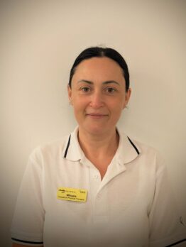 Headshot of a woman with long dark hair, wearing a white polo shirt with black trim and a yellow name tag.