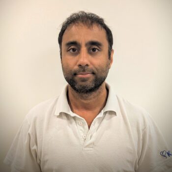 Headshot of a man with short dark hair and a beard, wearing a white polo shirt against a plain light background.