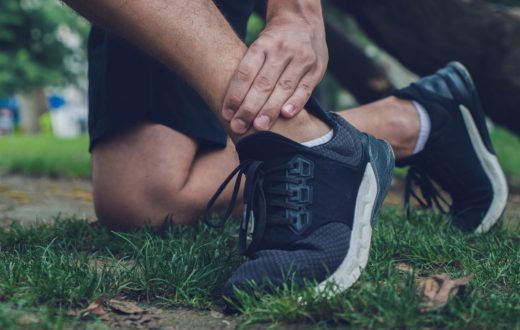 A close-up of a person kneeling on grass while clutching a painful ankle injury during an outdoor workout.
