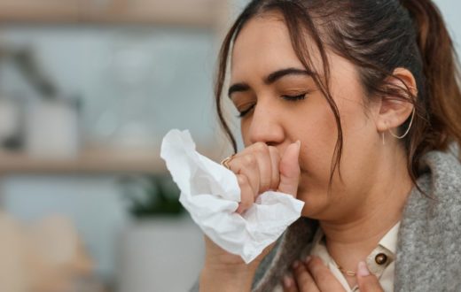 A young woman holds a tissue to her mouth while coughing, showing a typical reaction to respiratory discomfort.