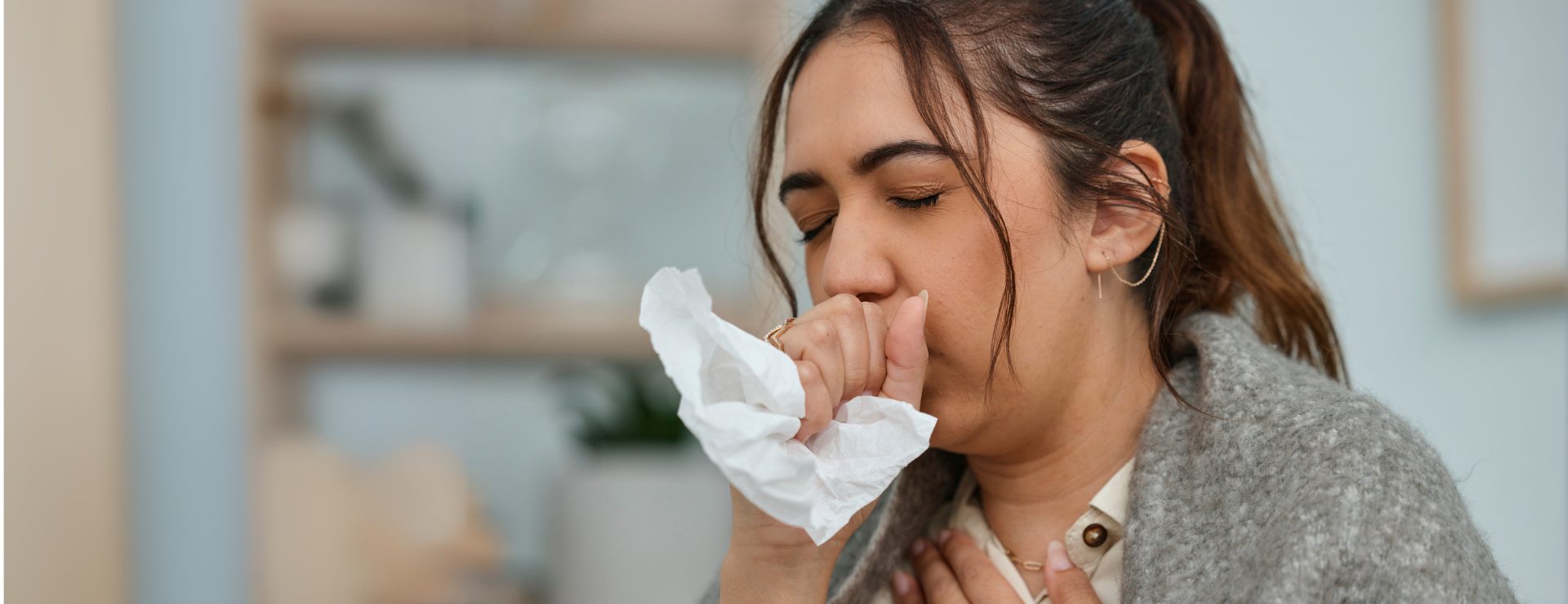 A young woman holds a tissue to her mouth while coughing, showing a typical reaction to respiratory discomfort.
