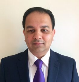 Professional photo of Dr. Vikram Sharma, a Gastroenterologist wearing a navy suit and purple tie against a plain wall.
