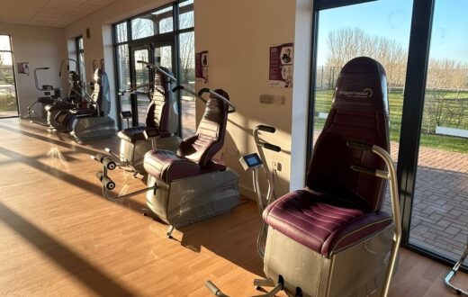 A row of Shapemaster power-assisted exercise machines in a bright KIMS Hospital gym with large windows and garden views.