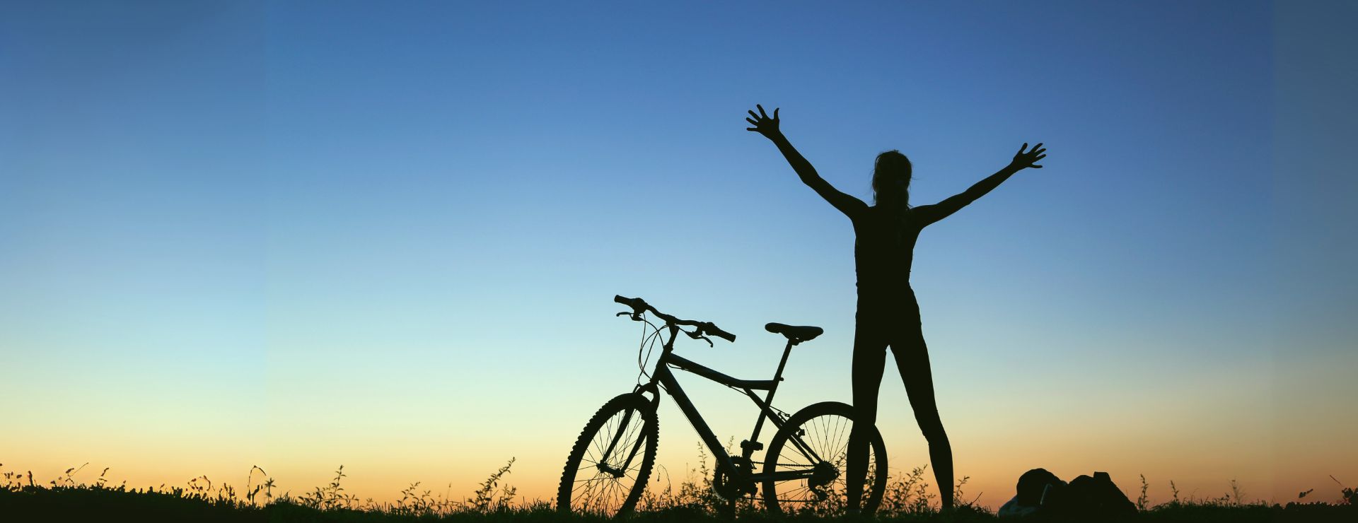 Silhouette of a person with a bicycle at sunrise, promoting health and wellbeing checks at KIMS Hospital in Kent.