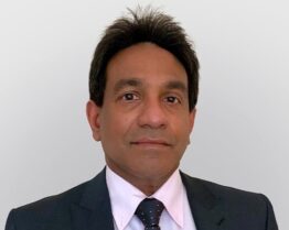 Professional headshot of Dr. Asankha Ranasinghe, wearing a dark suit, white shirt, and patterned tie against a wall.