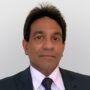 Professional headshot of Dr. Asankha Ranasinghe, wearing a dark suit, white shirt, and patterned tie against a wall.