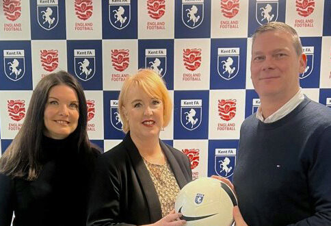 Three people holding a football in front of a Kent FA and England Football backdrop, promoting a health partnership.
